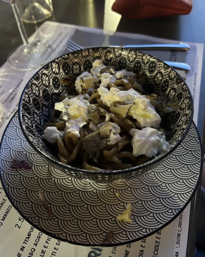 Ciotola di noodles con stracciatella e lamelle di tartufo nero, su un piatto decorato a onde.