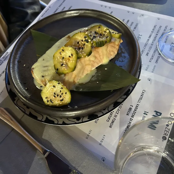 Trancio di salmone con zucchine al sesamo su una foglia verde, in un piatto scuro.