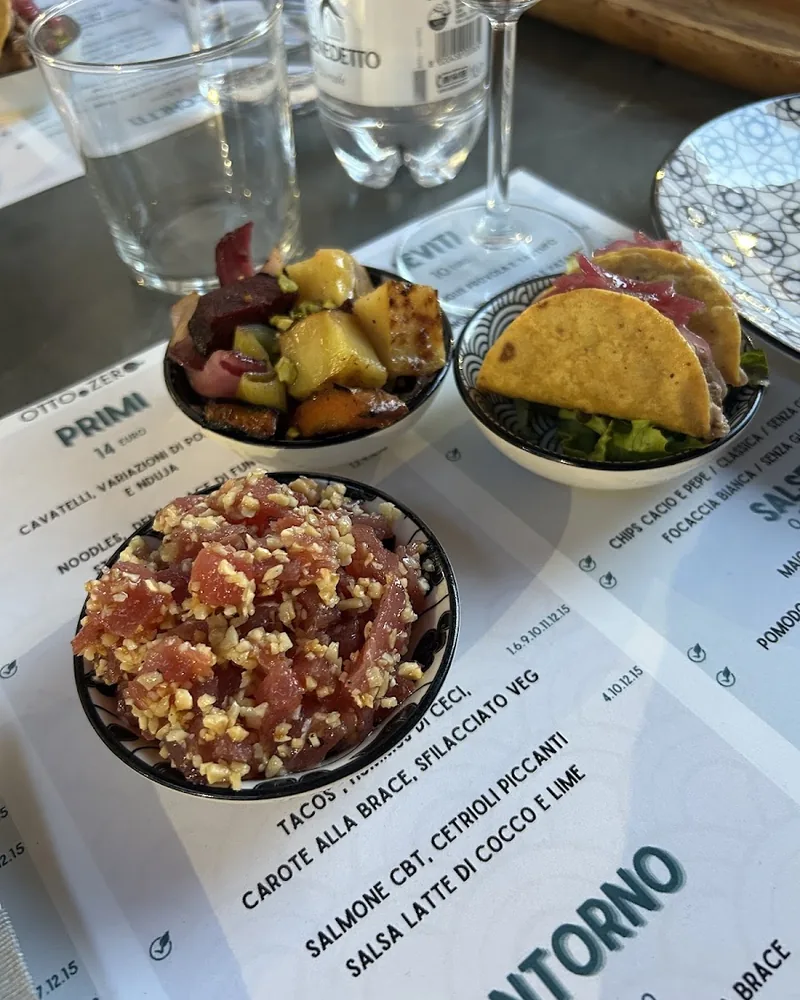 Tartare di tonno con granella di nocciole in una ciotolina, con due tacos e verdure alla brace dietro.