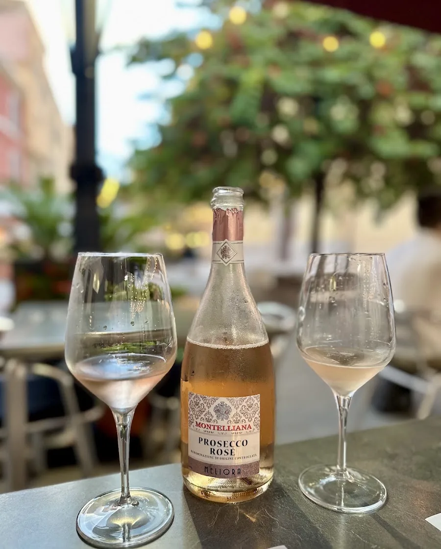 Bottiglia di prosecco rosé in ghiaccio e due calici su un tavolo in piazza, con l'albero illuminato dietro.